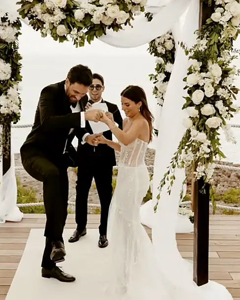 A groom breaking the glass under the chuppah as the bride smiles